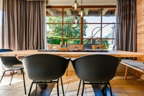 A dining area with a wooden table, black chairs, and a view of greenery through large windows. - Holiday apartment with 1 bedroom (Farchant)