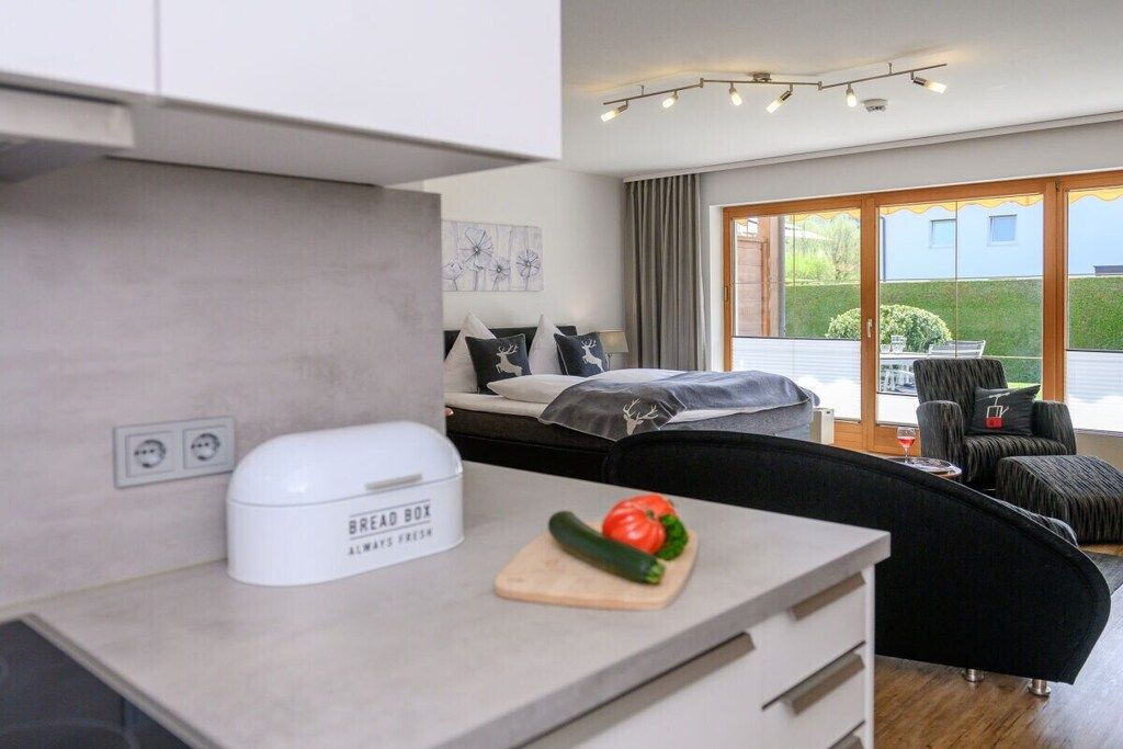 Cozinha moderna com um compartimento para pão, tábua de corte com legumes e uma cama com vista para o exterior.