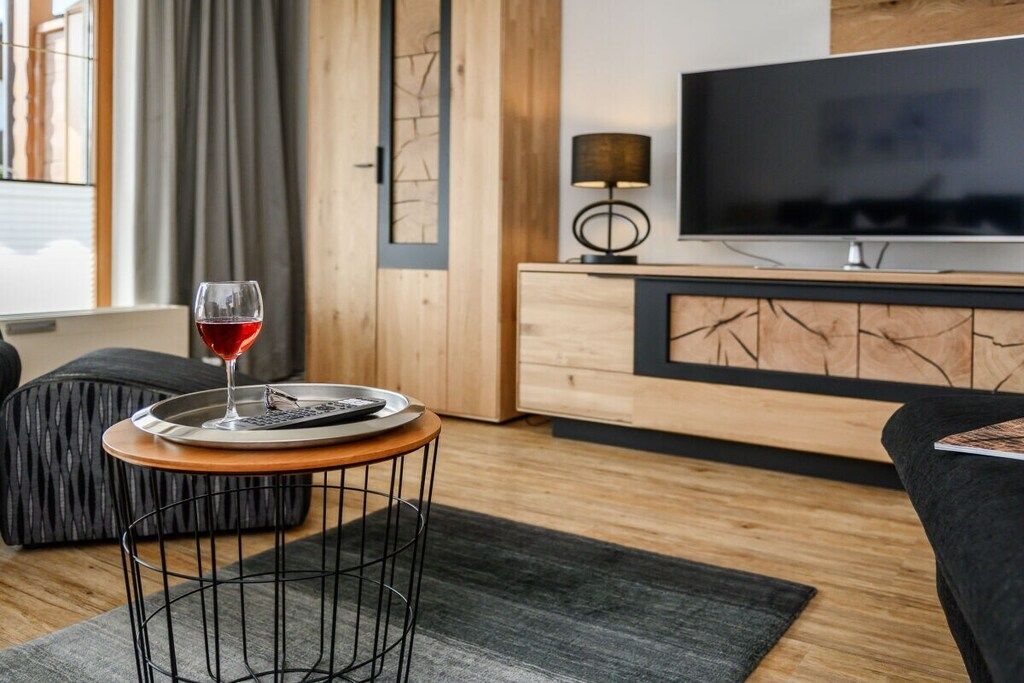 Una sala de estar moderna con televisor, una copa de vino tinto sobre un posavasos, una lámpara y un sofá.