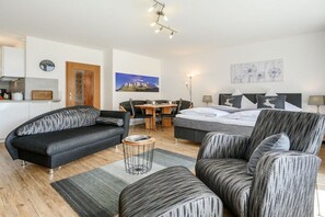 A modern bedroom with a bed, two sofas, a dining table, and a small kitchen area. - Holiday apartment with 1 bedroom (Garmisch-Partenkirchen)