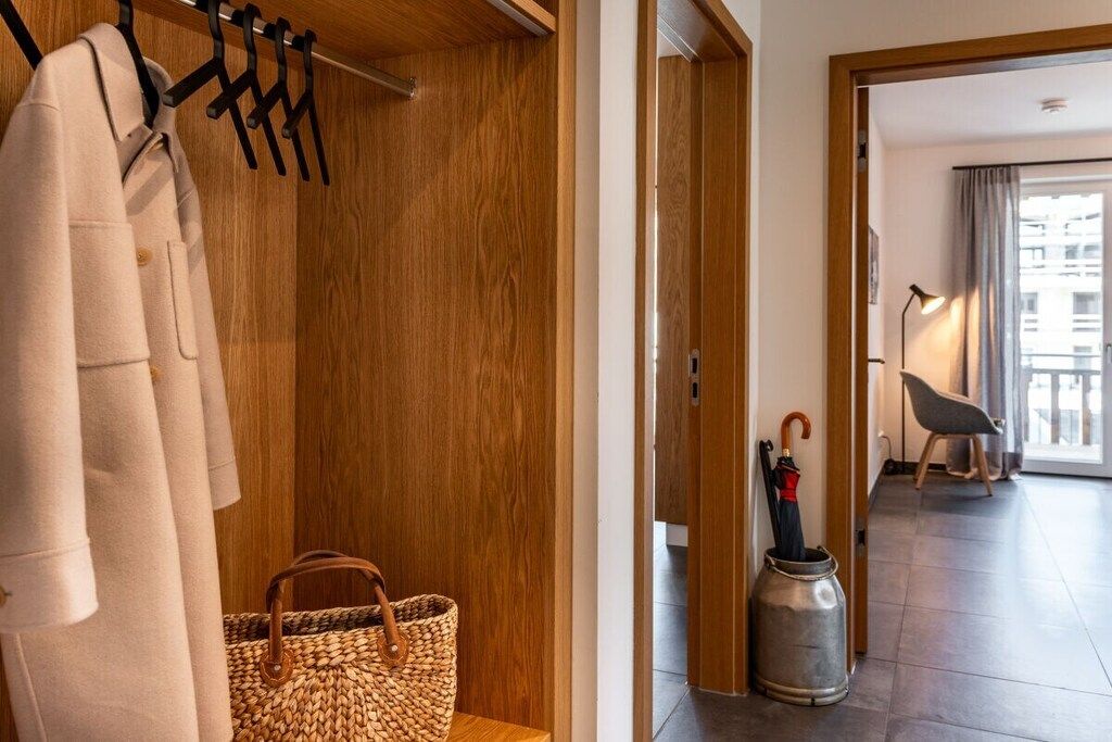Hotellihuoneessa on puinen vaatekaappi, kudottu laukku, metallinen ämpäri ja tuoli ikkunan vieressä.