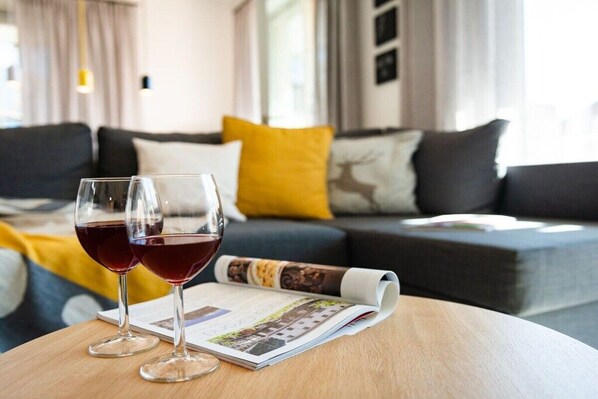 Een kamer met een bank, twee glazen rode wijn en een tijdschrift op een houten tafel.