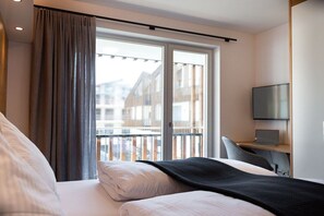 Een hotelkamer met een bed, een bureau met een laptop, een televisie en een balkon met uitzicht op gebouwen.