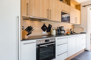 A modern kitchen with white cabinets, a stainless steel oven, and a black countertop. - Holiday apartment with 2 bedrooms (Garmisch-Partenkirchen)