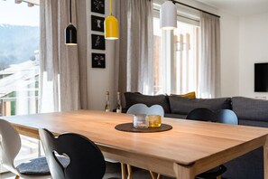 A dining area with a wooden table, black and white chairs, and a yellow pendant light. - Holiday apartment with 2 bedrooms (Garmisch-Partenkirchen)
