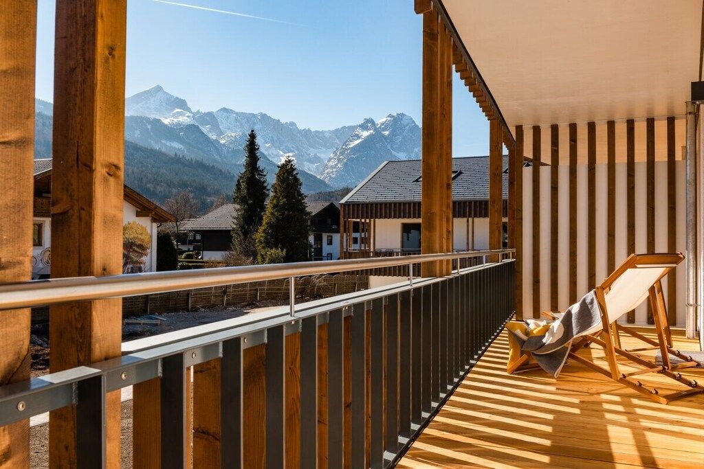 Une terrasse en bois offrant une vue sur des montagnes enneigées, avec un fauteuil de relaxation et une rambarde.