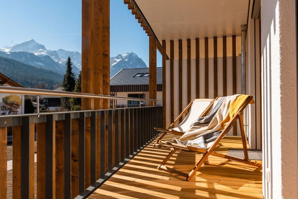 A balcony with a wooden floor, a metal railing, and a single lounge chair.