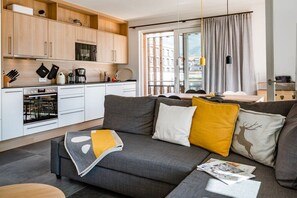 A modern living room with a grey sofa, a coffee table, and a kitchen area with white cabinets and appliances. - Holiday apartment with 2 bedrooms (Garmisch-Partenkirchen)