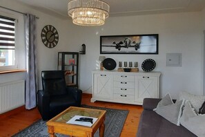 A living room with a black leather chair, a white cabinet with decorative items, a large framed picture, and a wooden coffee table. - Holiday apartment with 3 bedrooms (Föritztal)