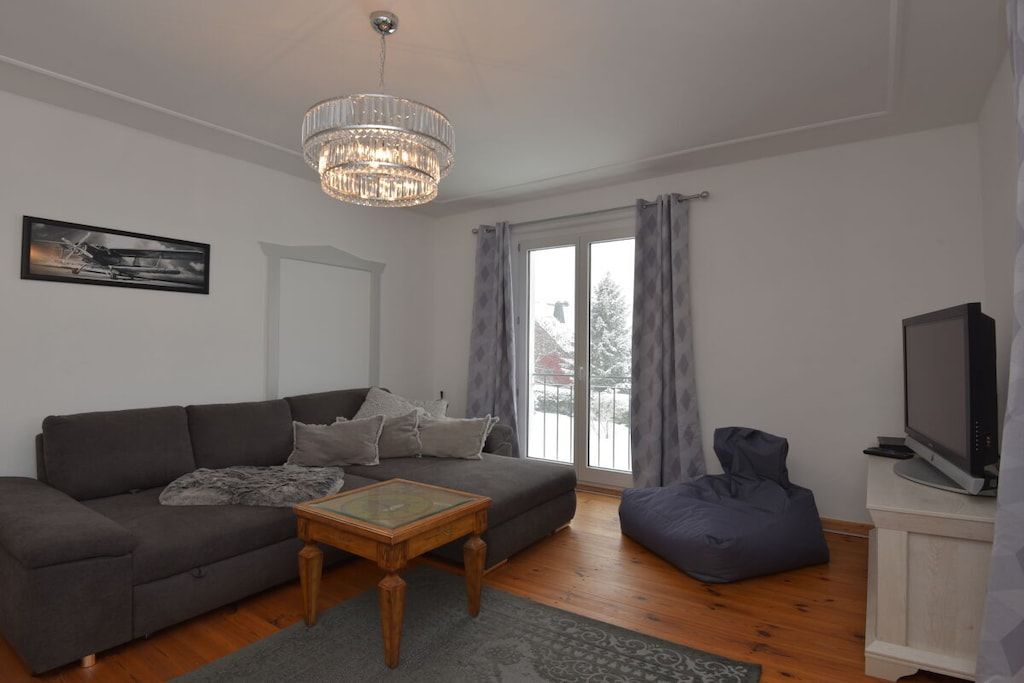 A living room with a sofa, a coffee table, a television, and a chandelier.