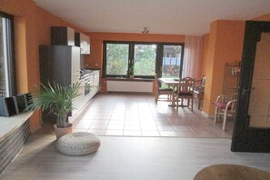 A spacious living area with a dining table and chairs, a potted plant, and a large window providing a view of the outdoors. - Holiday apartment with 3 bedrooms (Damscheid)