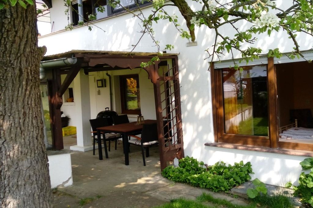 Un bâtiment blanc doté d’un patio couvert, d’une table à manger avec des chaises et d’une fenêtre donnant sur l’intérieur.