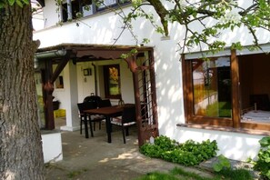 A white building with a covered patio area, a dining table with chairs, and a window with a view of the interior. - Holiday apartment with 3 bedrooms (Damscheid)