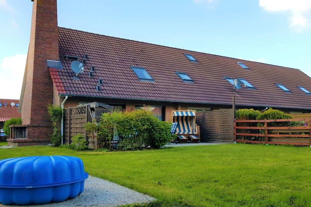 Ein Gebäude mit geneigtem Dach, einem Ziegelkamin und einem umzäunten Garten mit einem blauen Pool.