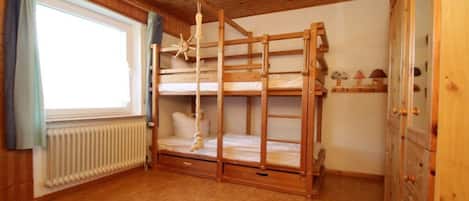 A bunk bed room with a wooden ceiling, a window with curtains, a radiator, and a wooden wardrobe.