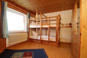 Ein Schlafraum mit Etagenbetten, Holzboden, einem Fenster mit Vorhängen, einem Heizkörper und einem Holzschrank.