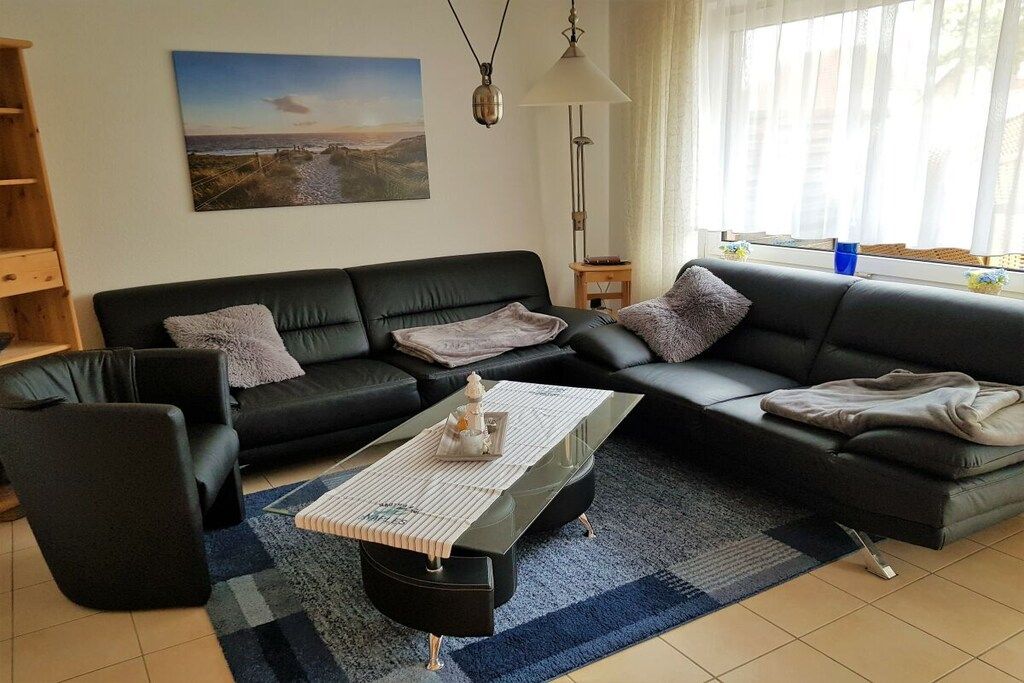 Una sala de estar moderna con un sofá de cuero negro, una mesa de centro de vidrio y una alfombra azul.