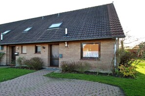 Ein zweistöckiges Haus mit Ziegeldach, einer Haustür und einem kleinen Garten.
