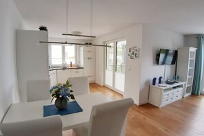 Une cuisine moderne avec des meubles blancs, une table à manger avec des chaises et un téléviseur posé sur un meuble blanc.