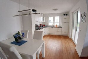 A modern kitchen with white cabinetry, a dining table with chairs, and a blue placemat. - Holiday apartment with 2 bedrooms (Breege\/Juliusruh OT Juliusruh)