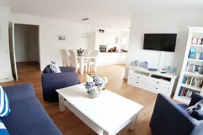 A modern living room with a sofa, a coffee table with flowers, a TV, and a bookshelf. - Holiday apartment with 2 bedrooms (Breege\/Juliusruh OT Juliusruh)