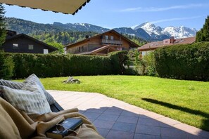 A patio area with a view of mountains and a wooden house in the background. - Holiday apartment with 2 bedrooms (Garmisch-Partenkirchen)