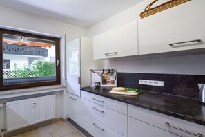 A kitchen with white cabinets, a black countertop, and a window with a view of greenery. - Holiday apartment with 2 bedrooms (Garmisch-Partenkirchen)