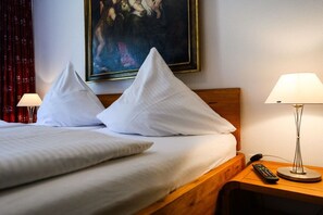Ein Hotelzimmer mit einem Bett, Kissen, einem Bild an der Wand, einer Lampe und einer Fernbedienung auf dem Nachttisch.
