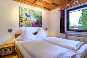 A hotel room with a bed, a painting on the wall, a window with curtains, and a radiator. - Holiday apartment with 2 bedrooms (Garmisch-Partenkirchen)