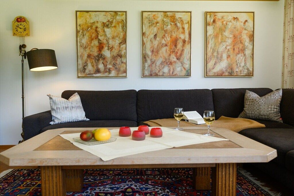Ein Wohnzimmer mit einer Couch, einem Couchtisch mit Früchten und Kerzen sowie abstrakten Bildern an der Wand.