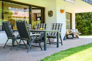 Eine Terrassengruppe mit Tisch und Stühlen, eine Bank und ein Fenster mit Blick auf einen Garten.