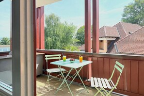 A balcony with a table and two chairs, a small plant, and a view of neighboring buildings. - Holiday apartment with 1 bedroom (Kressbronn am Bodensee)
