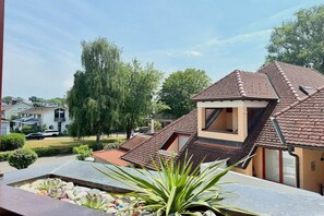 Il s’agit d’une propriété résidentielle dotée d’un toit en pente, d’un petit balcon et d’un jardin agrémenté de rochers et de plantes.