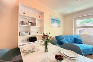 Un coin repas avec une table dressée pour deux personnes, un canapé bleu et une bibliothèque contenant divers objets.