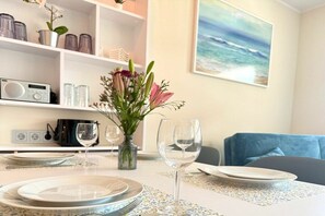 A dining area with a table set for two, a vase with flowers, and a painting of the ocean on the wall. - Holiday apartment with 1 bedroom (Kressbronn am Bodensee)