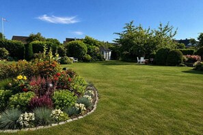A well-maintained garden with a lawn, various plants, and a white building in the background. - Garden apartment 283 (Lübeck-Travemünde)