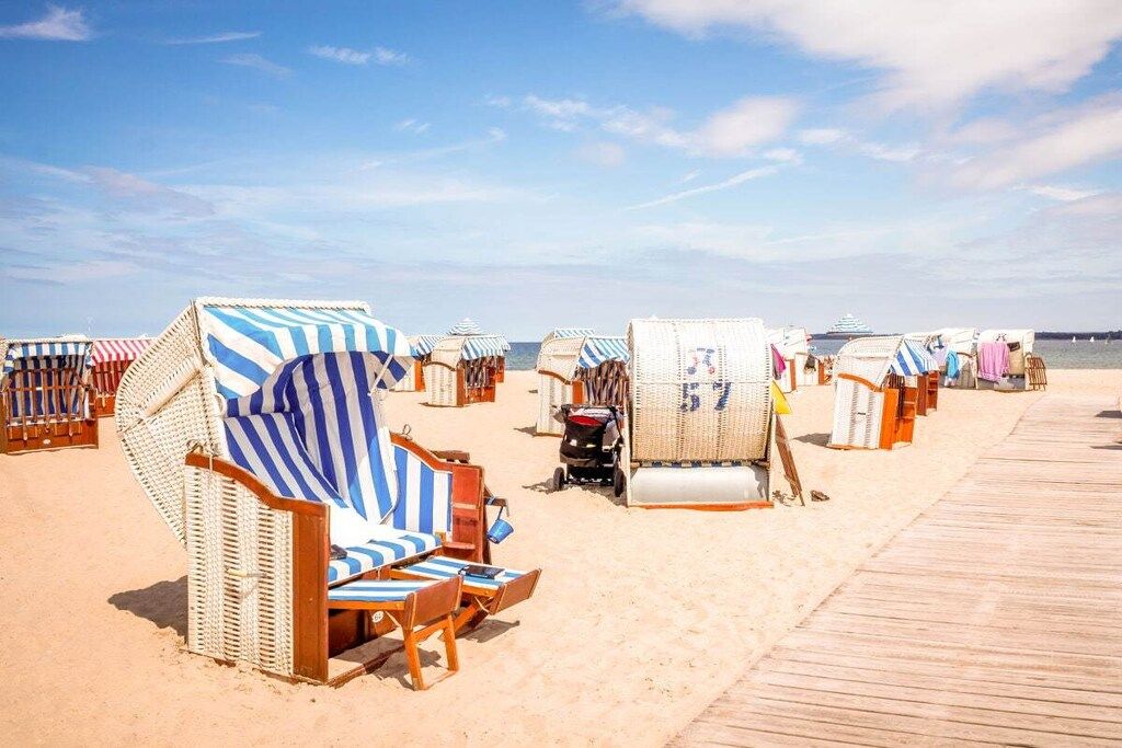 A beach with rows of beach chairs and umbrellas, a wooden boardwalk, and a distant ship.