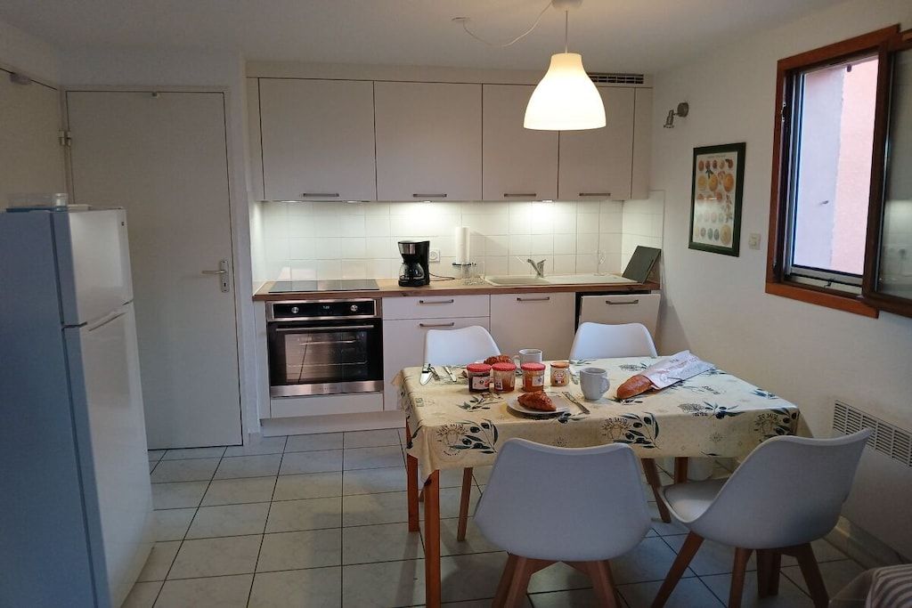 Une cuisine compacte avec des meubles blancs, une table à manger avec des chaises et un luminaire suspendu.