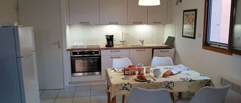 Une cuisine compacte avec des meubles blancs, une table à manger avec des chaises et un luminaire suspendu.