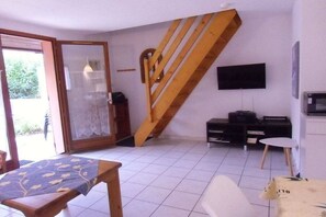 A room with a wooden staircase, a television mounted on the wall, a table with a tablecloth, and a chair. - Holiday home with 1 bedroom (Gruissan les Ayguades)