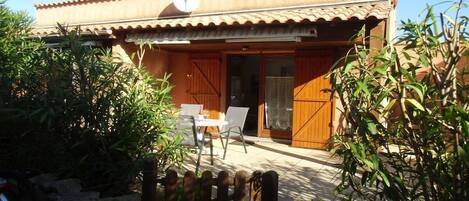 A building with a tiled roof, a satellite dish, and a wooden door. There is a patio with a table and chairs.
