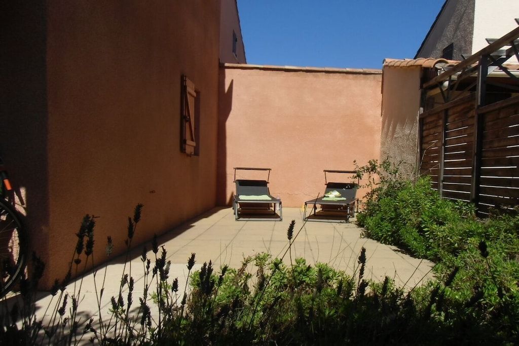 A courtyard with two lounge chairs, a bicycle, and a building with a sloped roof.