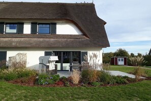 Ein Haus mit einem steilen Satteldach, einer Veranda mit einem Stuhl und einem kleinen Schuppen im Hintergrund.