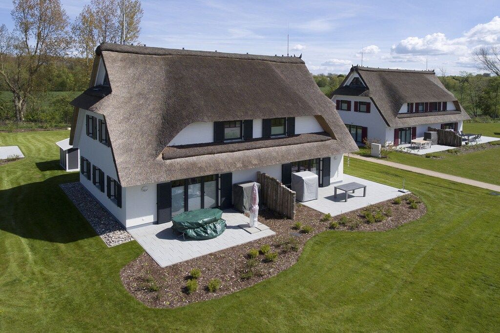 Ein modernes Haus mit Strohdach, großen Fenstern und einem gepflegten Rasen.