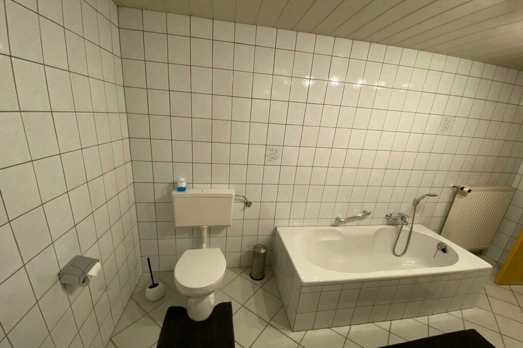 Ein Badezimmer mit weißen Fliesen, einer Toilette, einem Waschbecken und einer Badewanne.