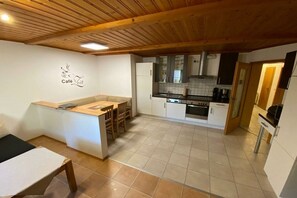 Cozinha com teto de madeira, armários brancos e chão de azulejos.