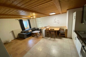 A cozy living room with a sofa, a dining table, and a kitchen area with a refrigerator and stove. - Holiday apartment in Langdorf with barbecue (Langdorf)