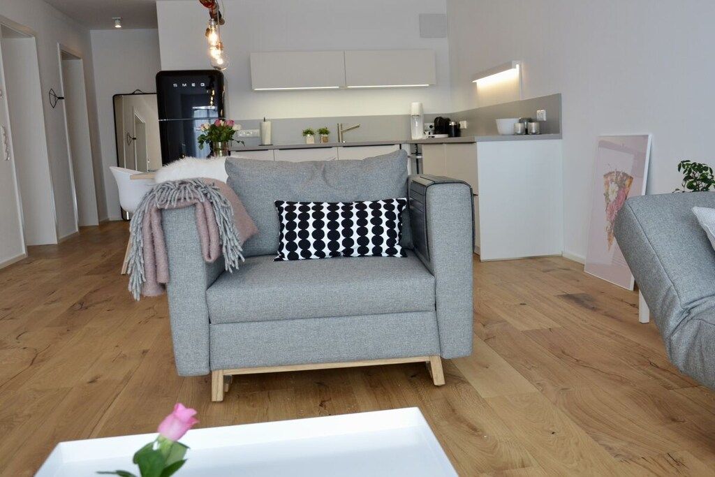 Una sala de estar moderna con un sofá gris, una mesa de centro blanca y una cocina al fondo.