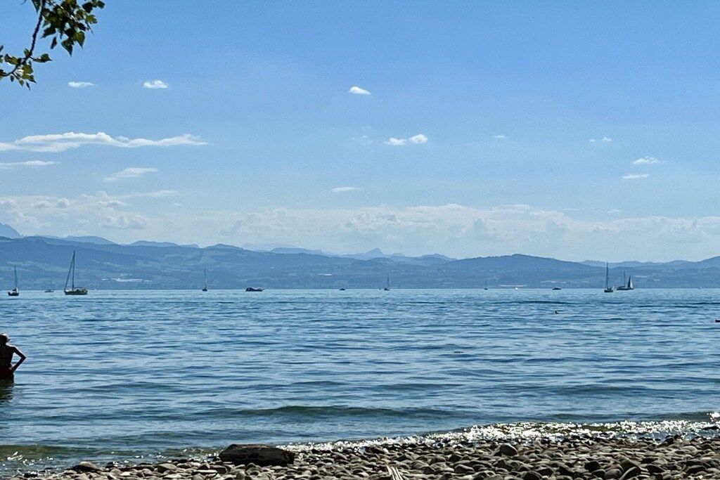 A calm lake with boats, a rocky shoreline, and distant mountains.