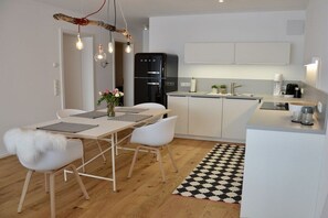Eine moderne Küche mit weißen Schränken, einem schwarzen Kühlschrank und einem Essbereich mit einem Holztisch und weißen Stühlen.